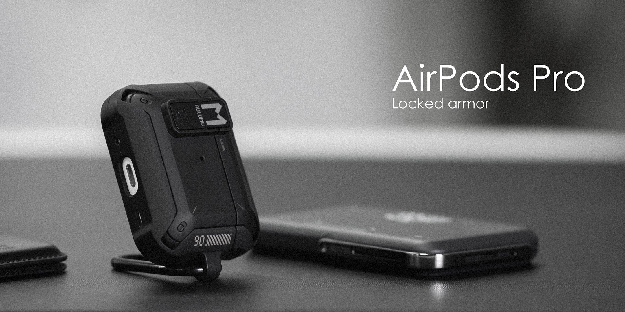 aulumu A19 AirPods Pro用ロック付き耐衝撃ケースをデスクの上に立てたモノクロイメージ スマホと一緒に写した「Locked armor」コンセプトショット